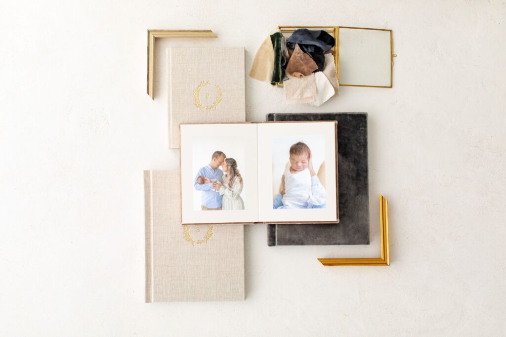 A matted album laying open on top of additional albums varying in size and album material designed by a Raleigh newborn photographer. 