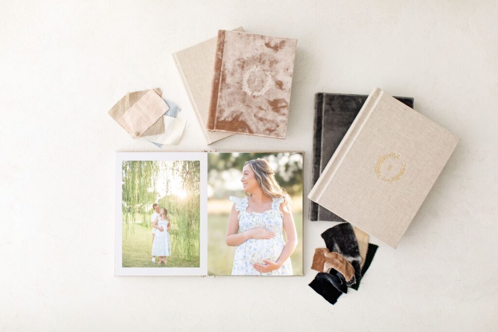 An heirloom album displaying maternity photos of a young couple standing below a gorgeous green willow tree and backlit by the sun and a photo of a mother looking off camera and holding her belly. 