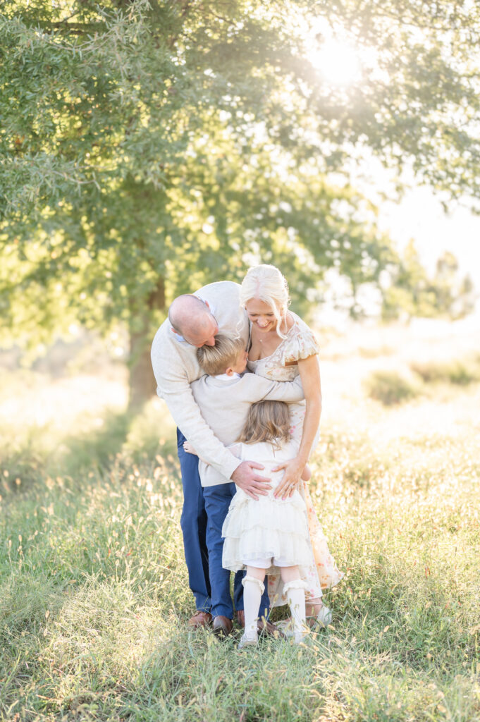 A young family of four embracing in a family hug with the golden sun setting behind them.